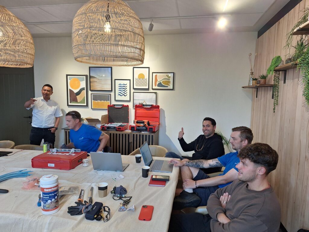 Image of Voicepath colleagues sat around table receiving instruction from Hilti representative. Laptops and sample tools on the table.